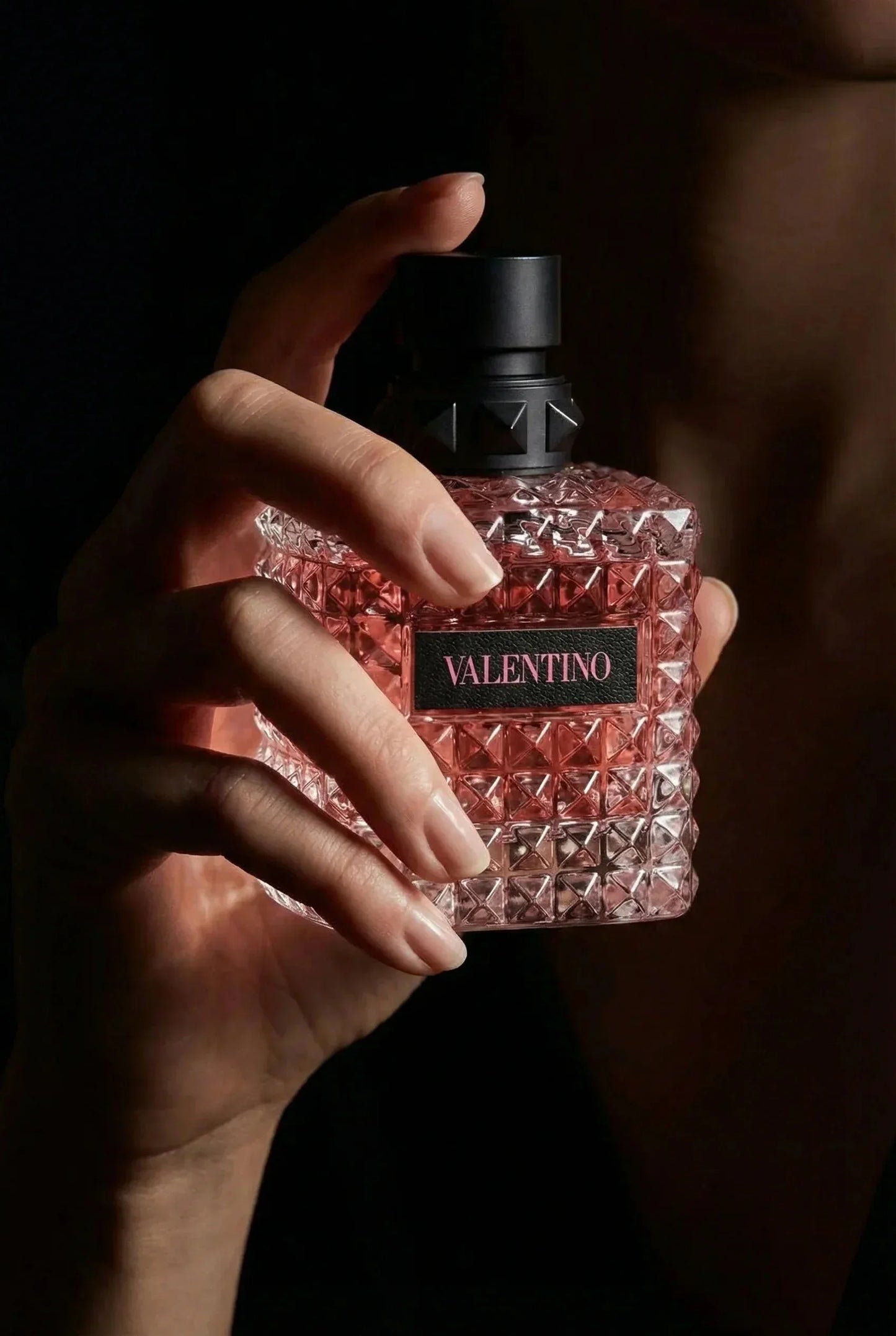 Nahaufnahme einer Hand, die einen eleganten, rosafarbenen VALENTINO Parfumflakon hält