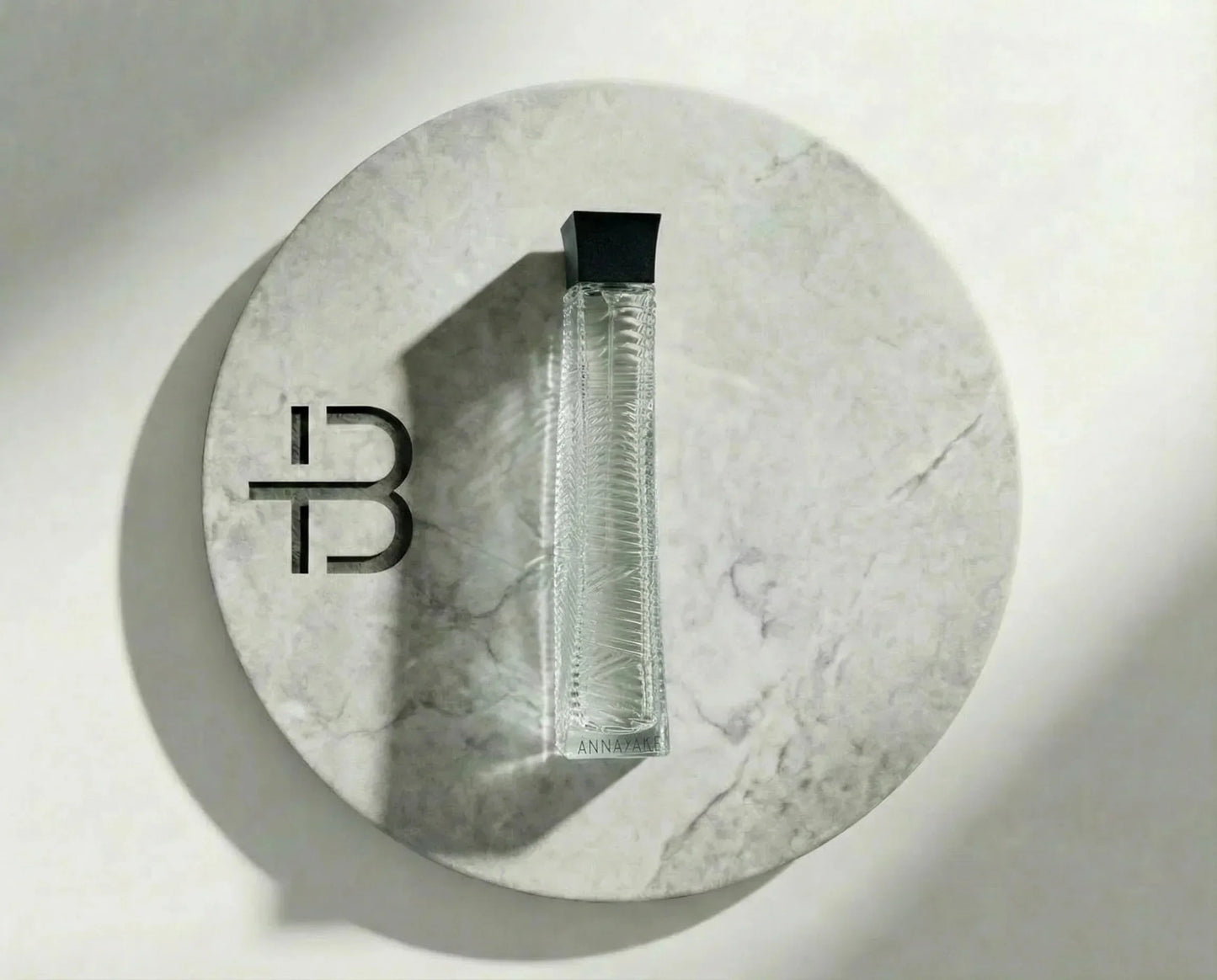 Eleganter Parfumflakon aus Glas mit schwarzem Deckel auf rundem Marmor-Untergrund, Luxusduft