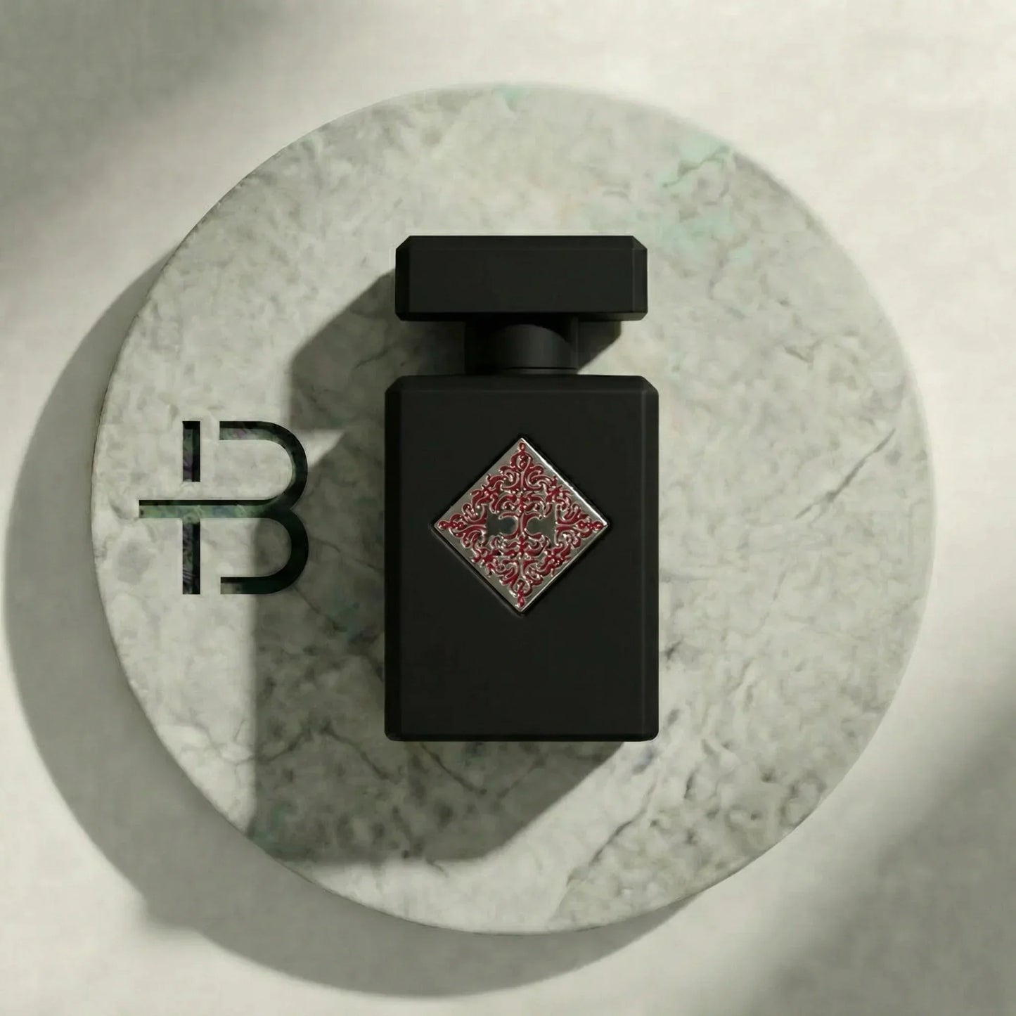 Edles schwarzes Parfumflakon mit rotem Ornament auf rundem Marmortablett, Luxusduft