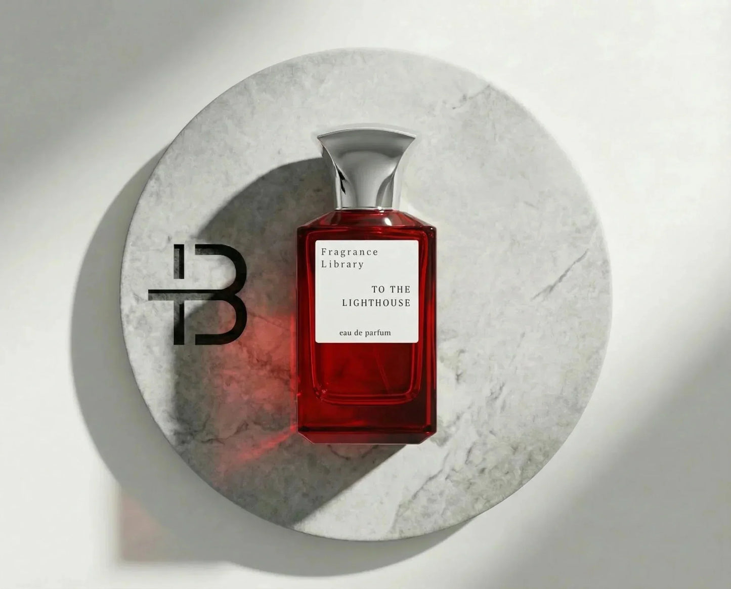 Rotes Parfumflakon mit silbernem Deckel und Label 'To The Lighthouse' auf Marmorteller