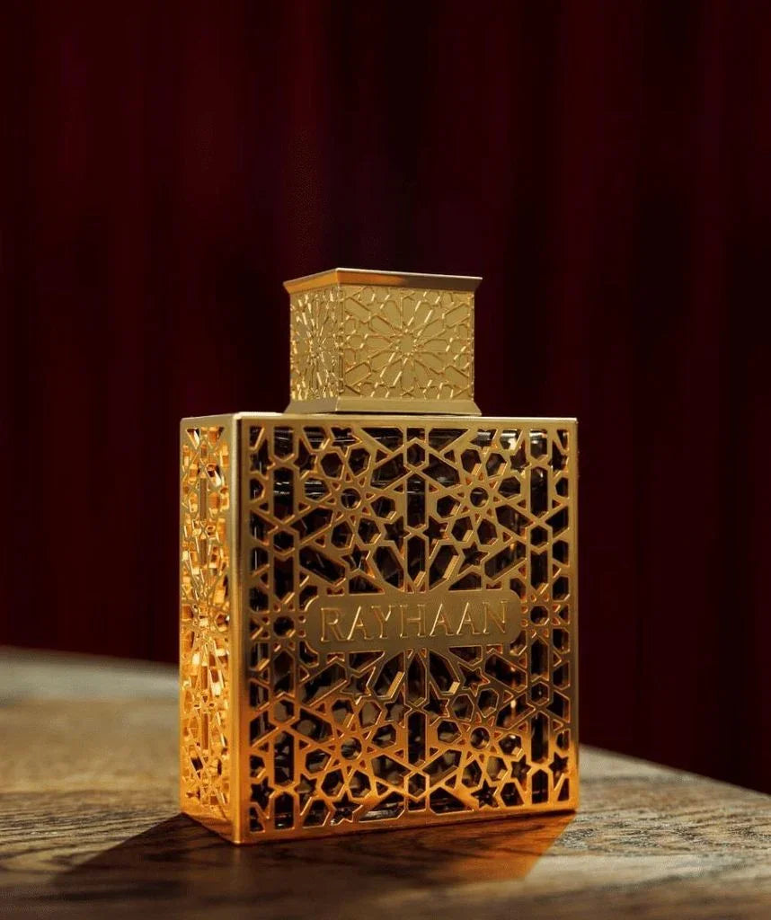 Luxuriöses Parfumflakon aus Gold mit orientalischem Muster und RAYHAAN-Schriftzug, auf Holztisch