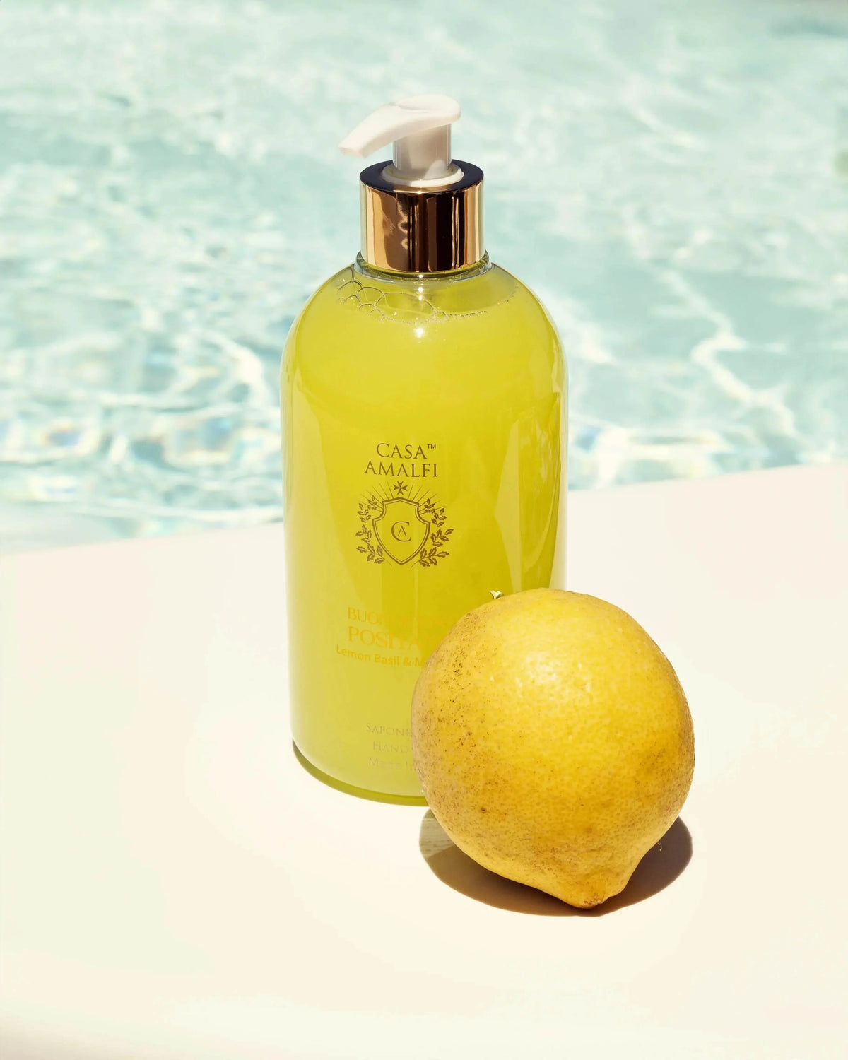 Casa Amalfi Buongiorno Positano Hand Wash in gelber Flasche mit einer Zitrone vor einem Pool.