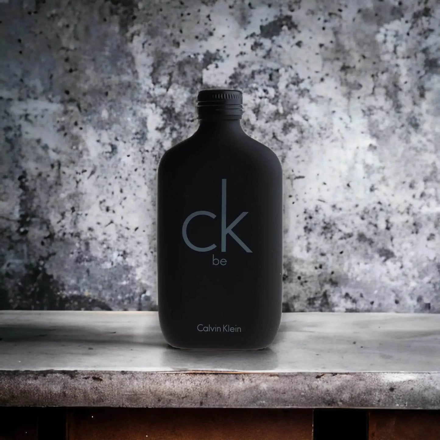 Schwarzer Flakon CK Be Eau de Toilette für Herren und Unisex auf grauem Hintergrund