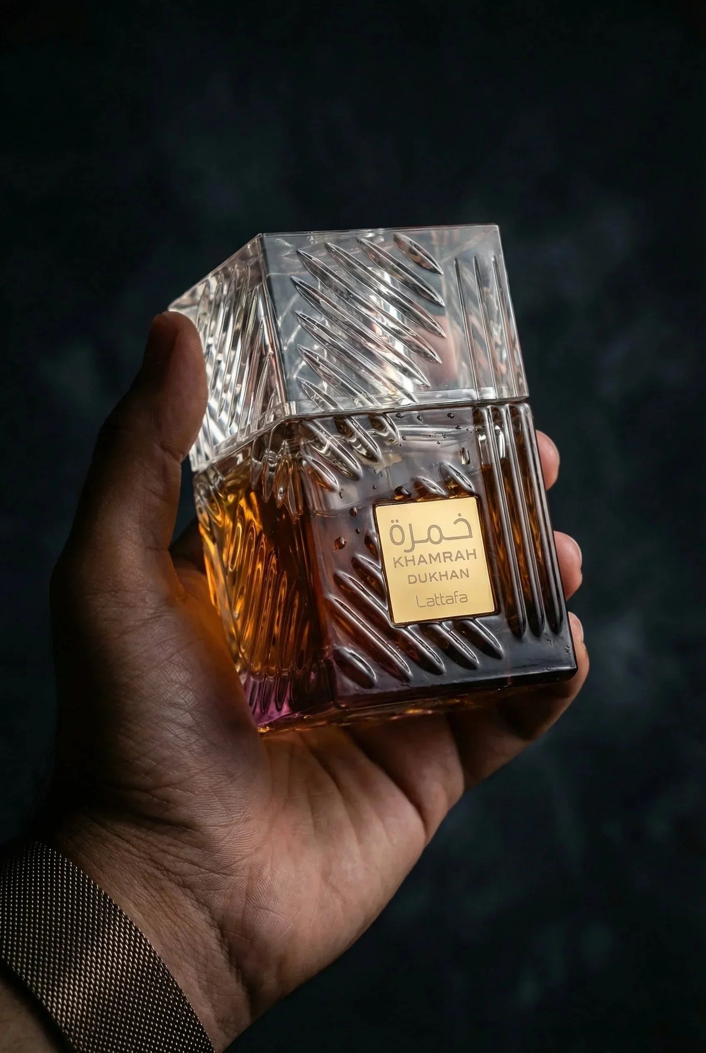 Nahaufnahme eines eleganten Parfümflakons Khamrah Dukhan von Lattafa in einer Hand, luxuriöses Design mit goldfarbenem Etikett.