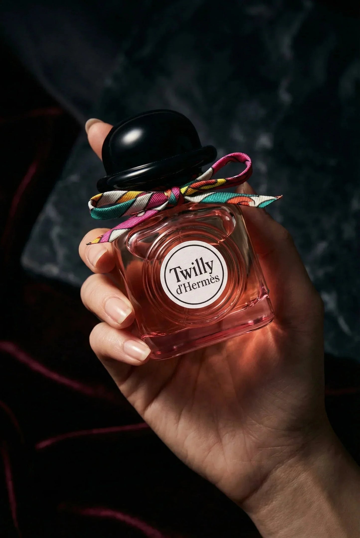 Hand hält eleganten Damenparfum-Flakon mit schwarzem Deckel und bunter Schleife, Nahaufnahme