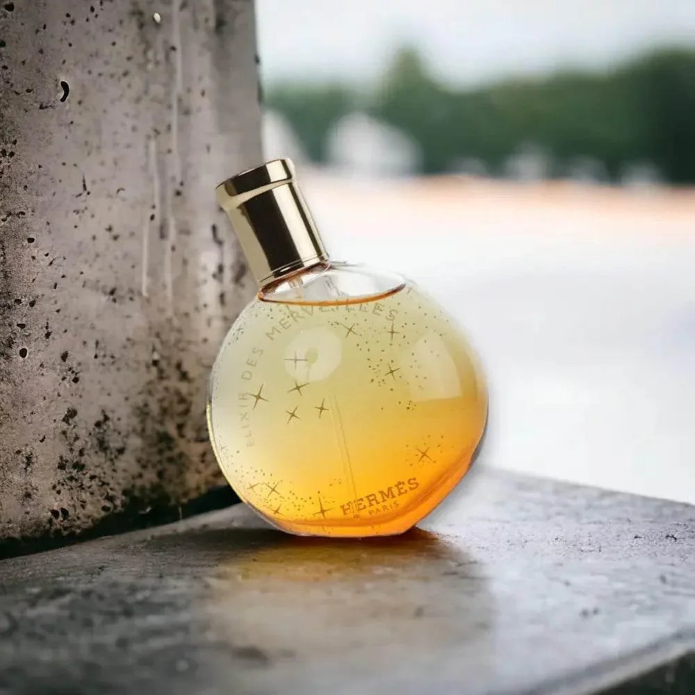 Rundes Parfümflakon mit goldener Kappe, orangefarbenes Luxusparfum auf Steinfläche