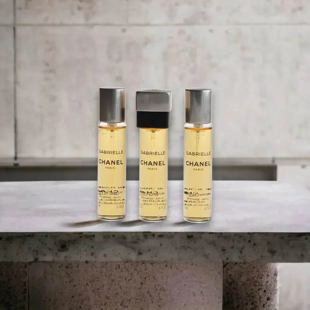 Drei Flakons Gabrielle Chanel Twist & Spray Eau de Parfum auf Steintisch, Luxusduft
