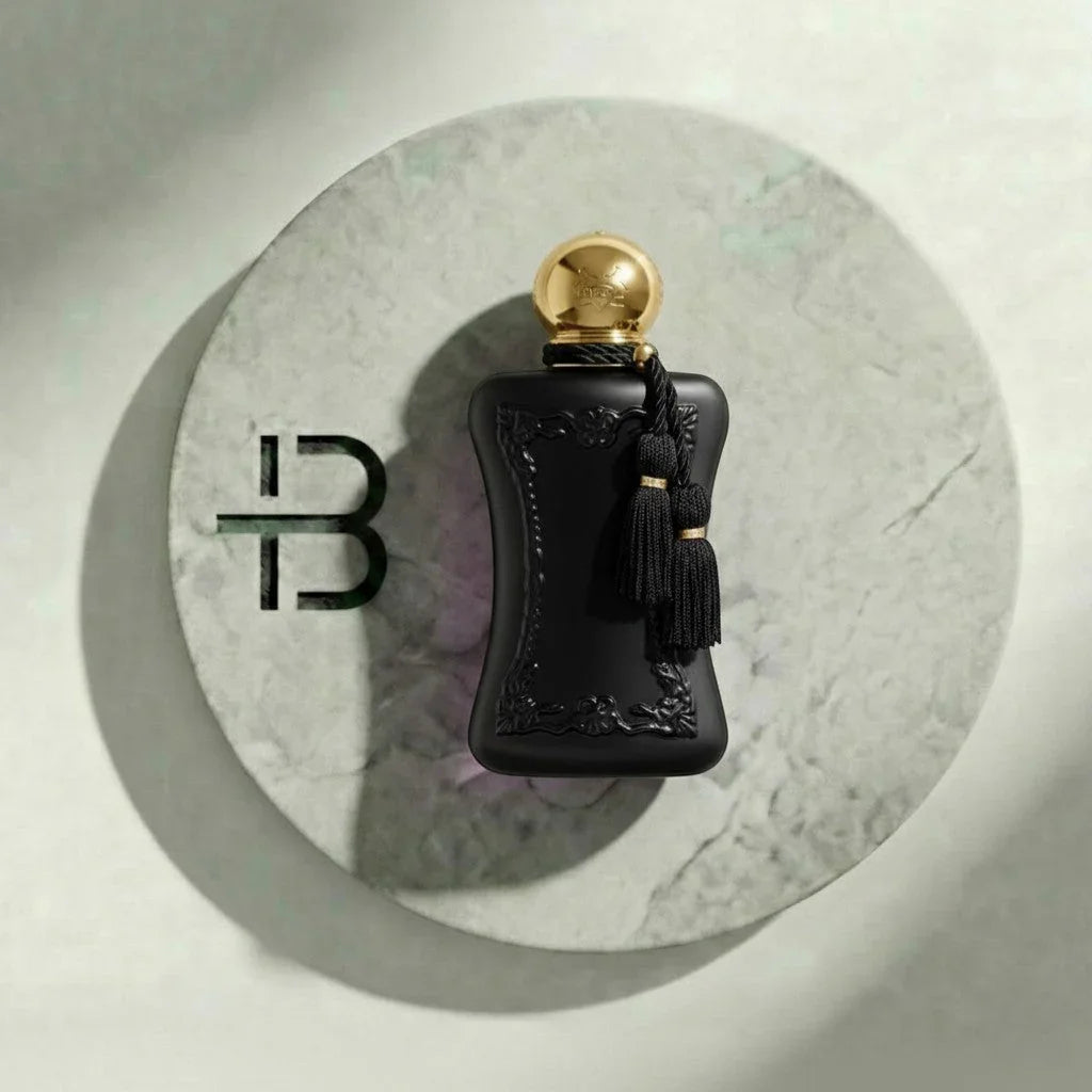 Edles schwarzes Parfumflakon mit goldener Kappe und Quasten auf rundem Marmoruntergrund
