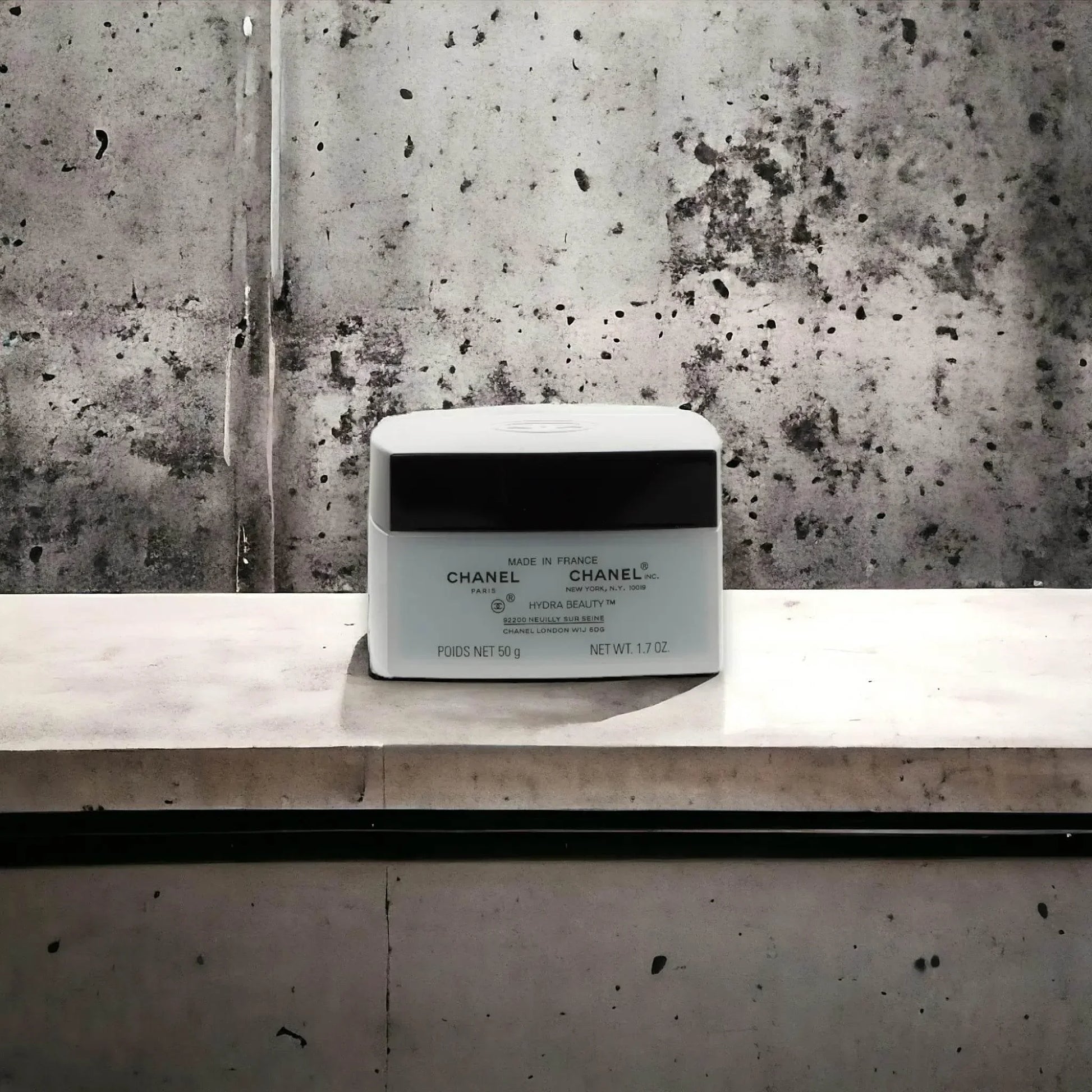 Luxuriöse Chanel Gesichtscreme in quadratischem Tiegel vor grauem Betonhintergrund
