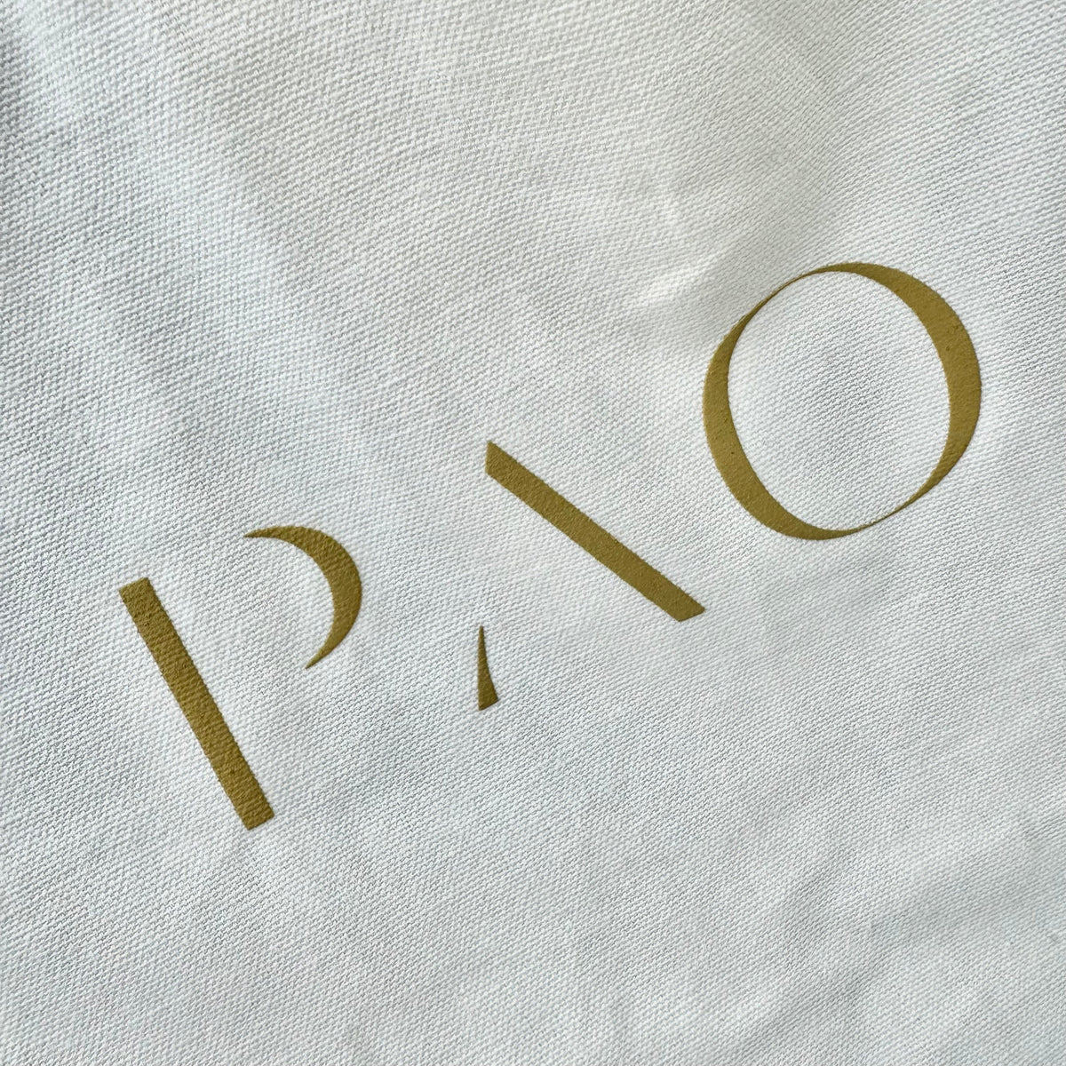 Nahaufnahme der goldenen Aufschrift auf einer weißen Tote Bag von paopao essentials.