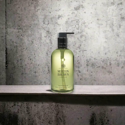 Transparente Flasche flüssige Handseife mit grünem Inhalt und Pumpspender vor Betonwand