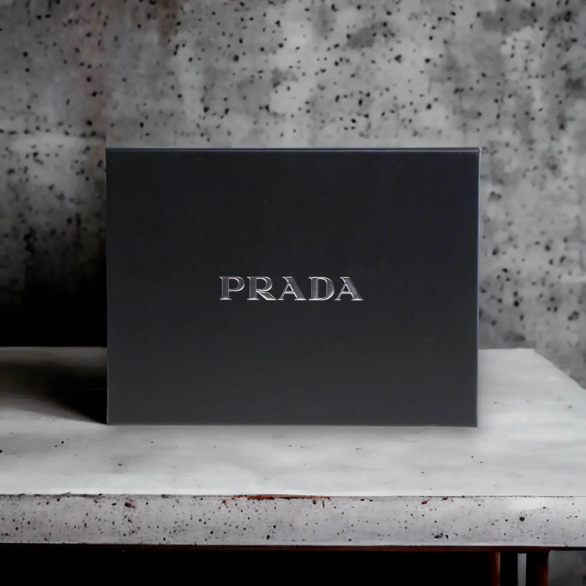 Edle schwarze PRADA Geschenkbox, luxuriöses Parfum Set auf hellem Tisch vor Steinwand.