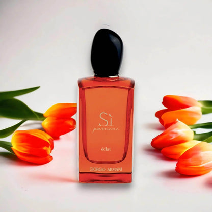 Rotes Parfumflakon mit schwarzem Deckel, Si Passione éclat, umgeben von orange-gelben Tulpen.