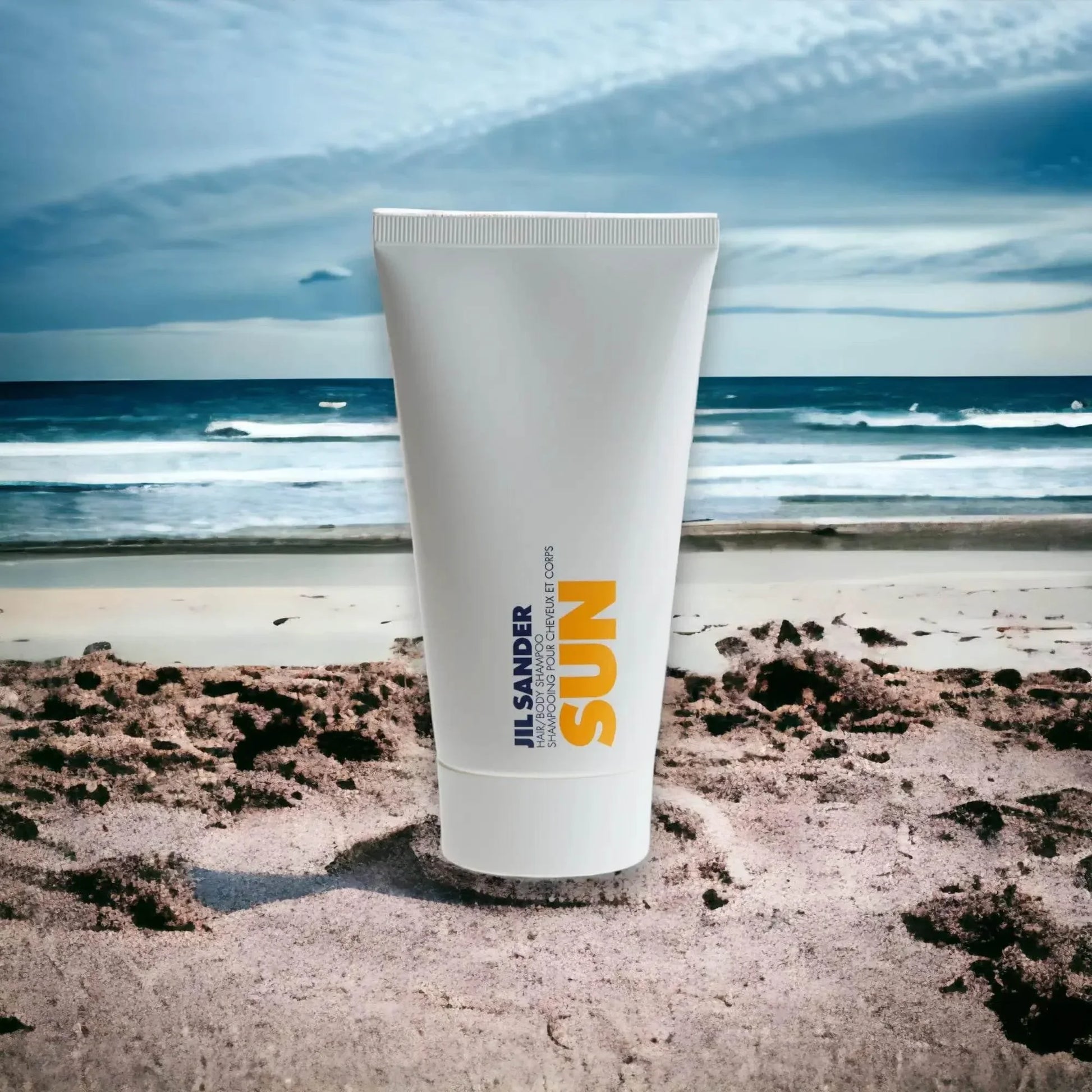 Jil Sander Sun Hair & Body Shampoo auf Sandstrand vor Meer mit blauem Himmel