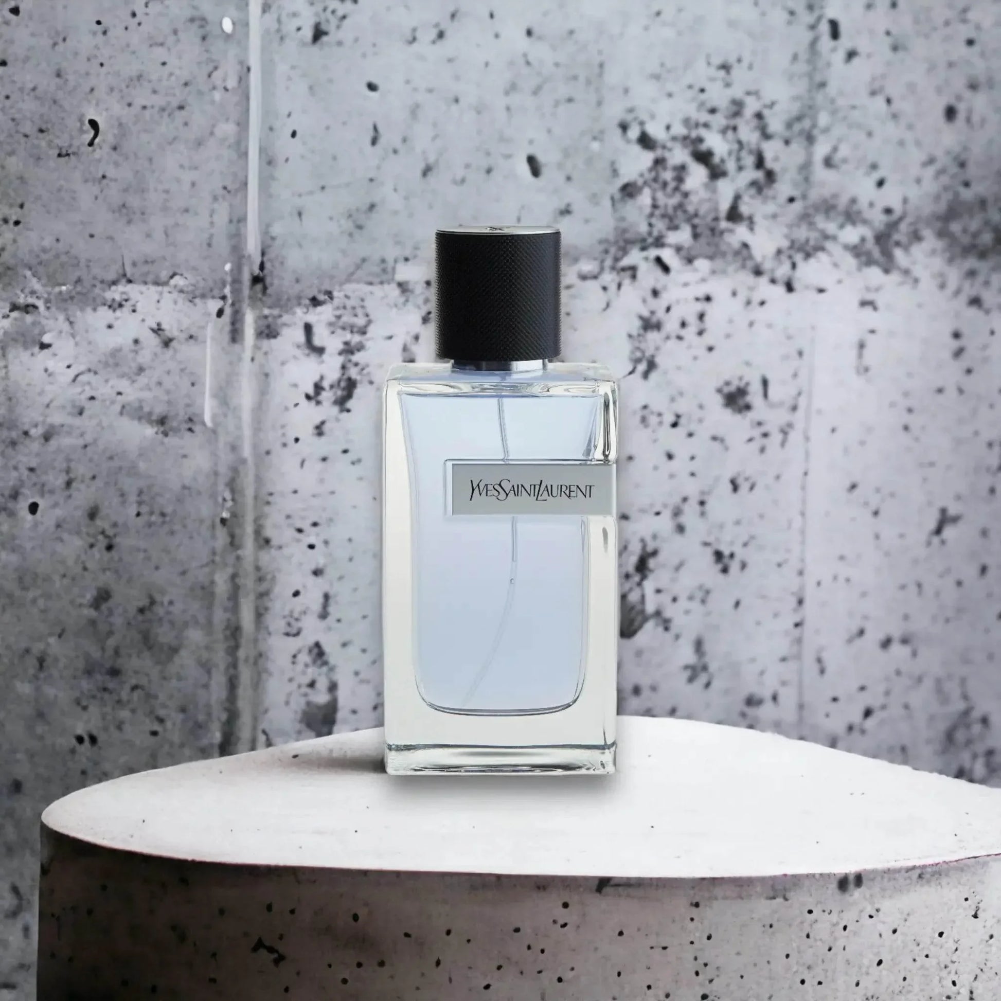 Edles Herrenparfum in klarem Glasflakon vor grauem Beton-Hintergrund