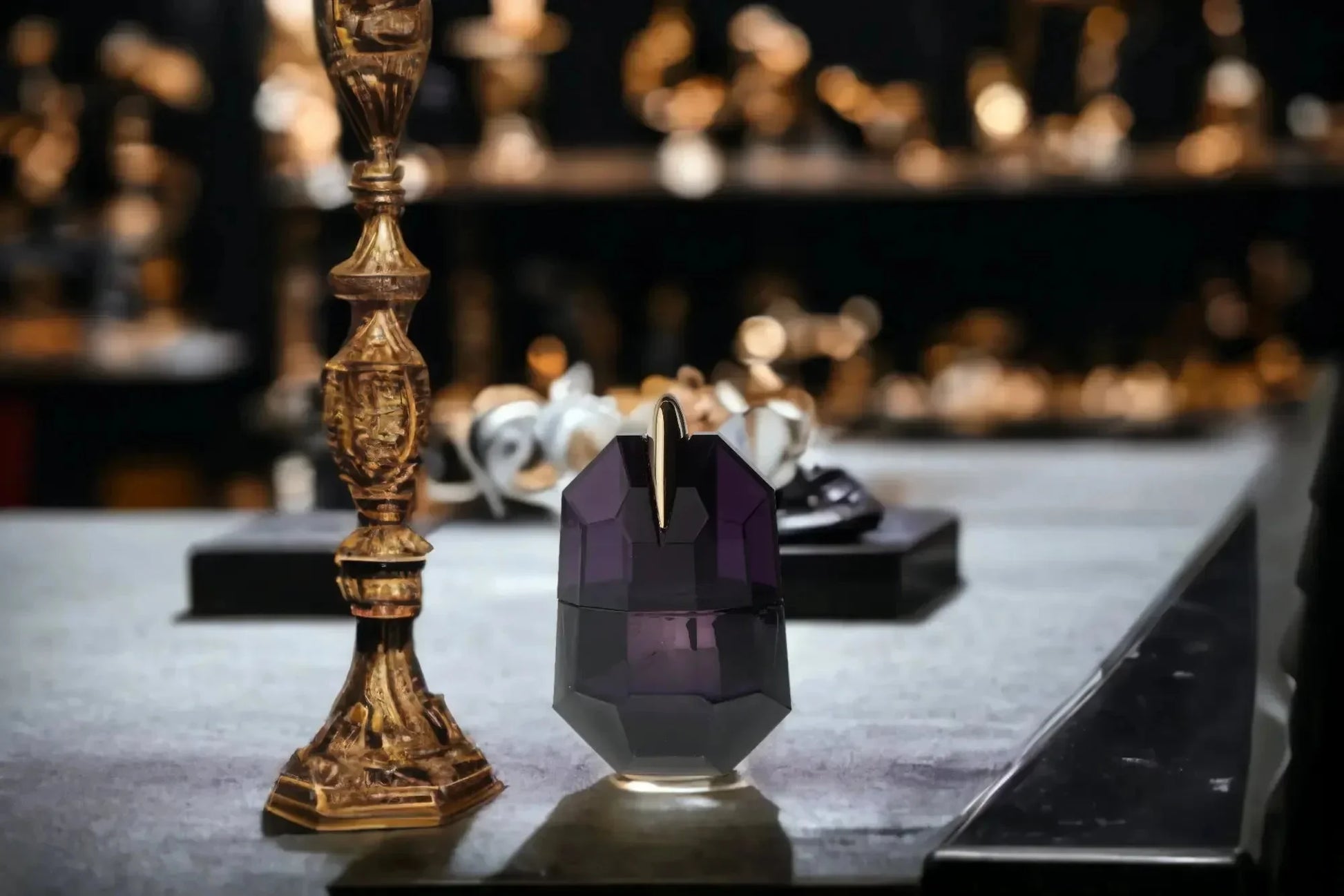 Lila Parfumflakon mit goldenen Akzenten neben verziertem Kerzenständer auf Tisch, luxuriöses Ambiente.