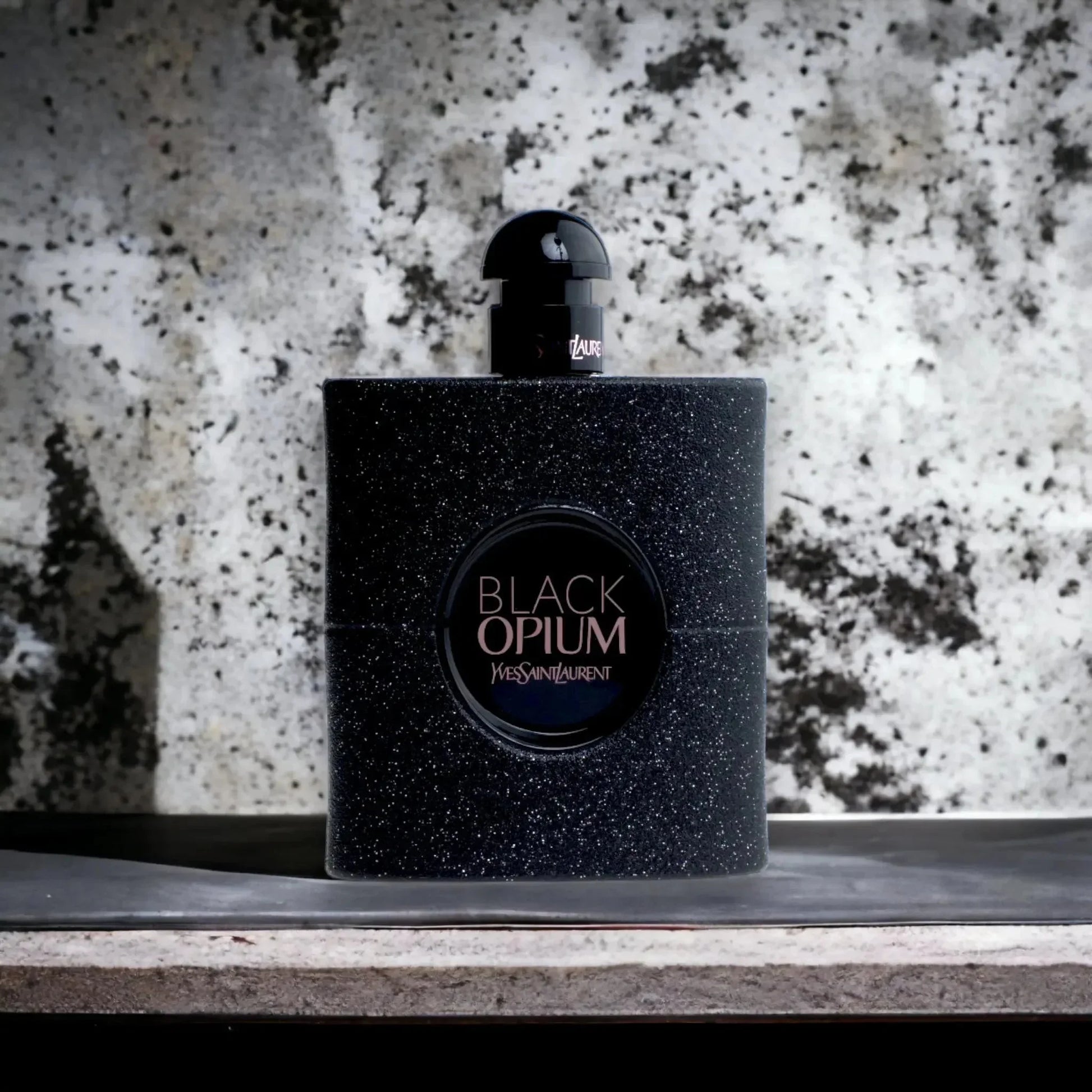 Luxuriöses schwarzes Parfumflakon Black Opium mit Glitzereffekt vor Marmorhintergrund