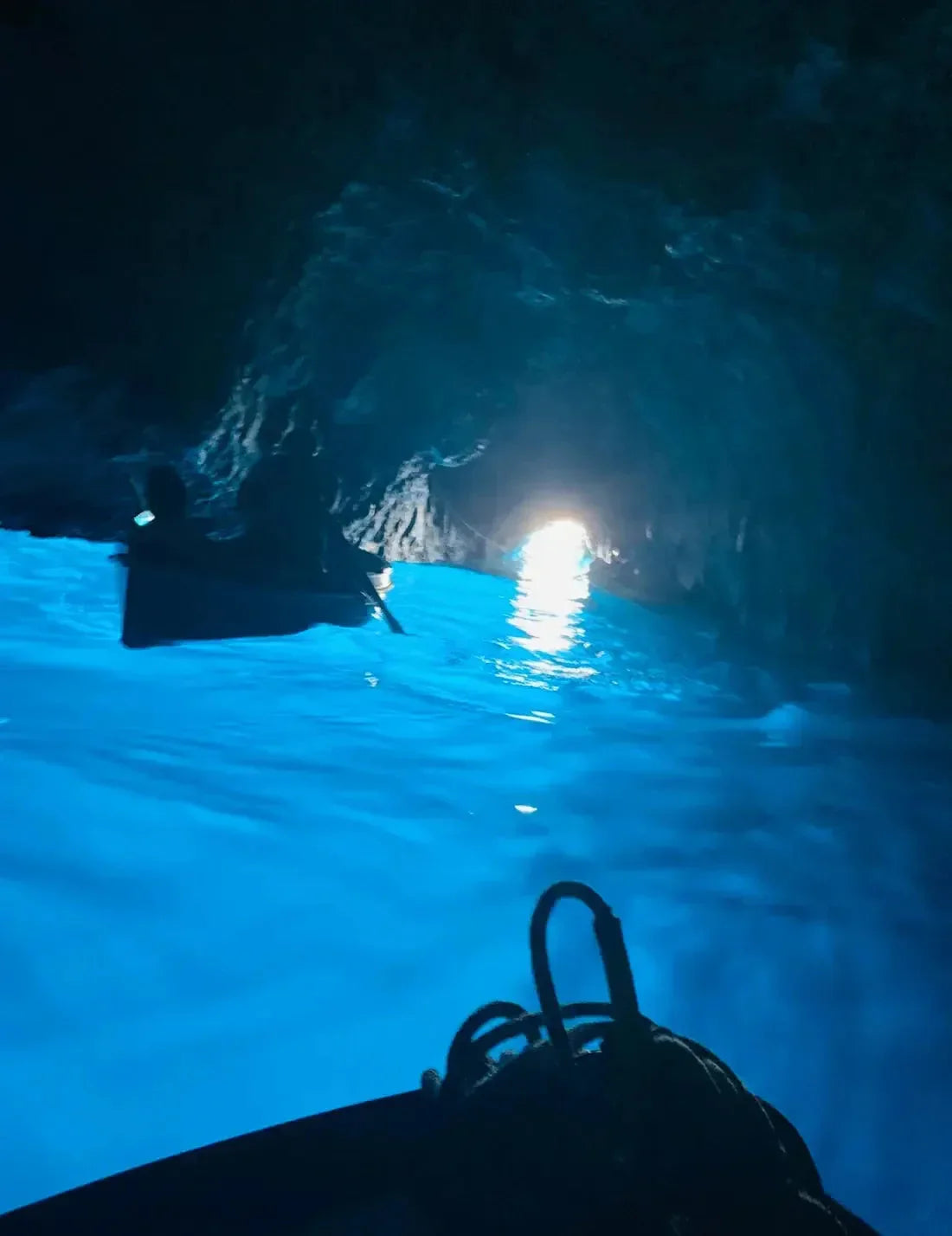 Blick aus einer Höhle mit leuchtend blauem Wasser und Booten auf dem Meer bei Tageslicht