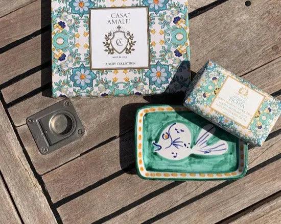 Luxuriöses Seifenset mit handbemalter Keramik-Seifenschale und floral verzierten Geschenkverpackungen auf Holztisch.