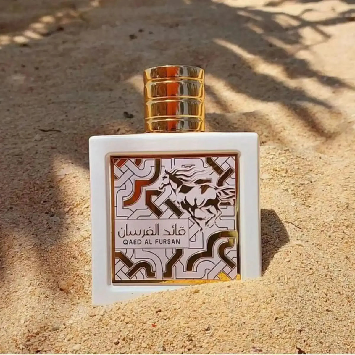 Luxusparfum Flakon mit goldener Kappe und orientalischem Muster steht im Sand, Aufschrift Qaed Al Fursan