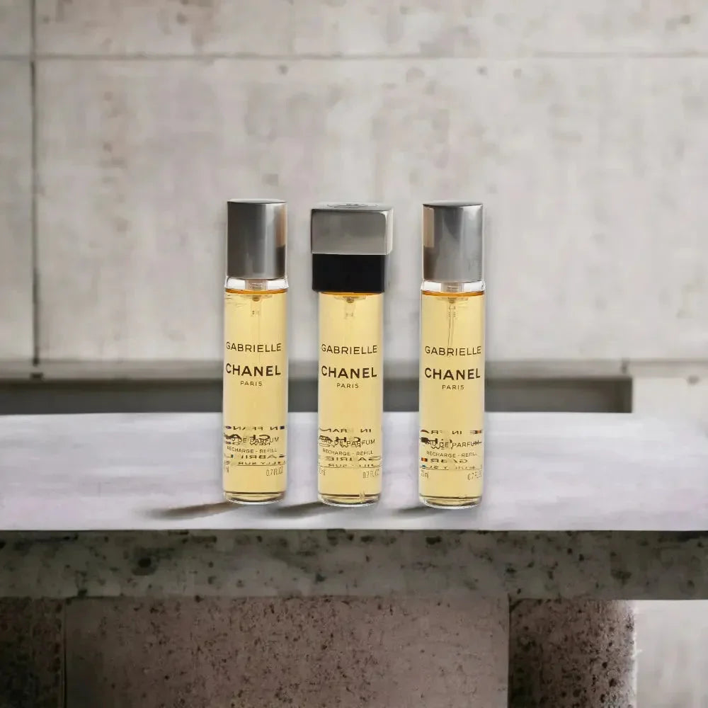 Drei Flakons Gabrielle Twist Spray Eau de Parfum stehen auf grauer Steinfläche