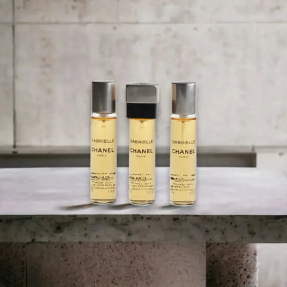 Drei Flakons Gabrielle Twist Spray Eau de Parfum stehen auf grauer Steinfläche