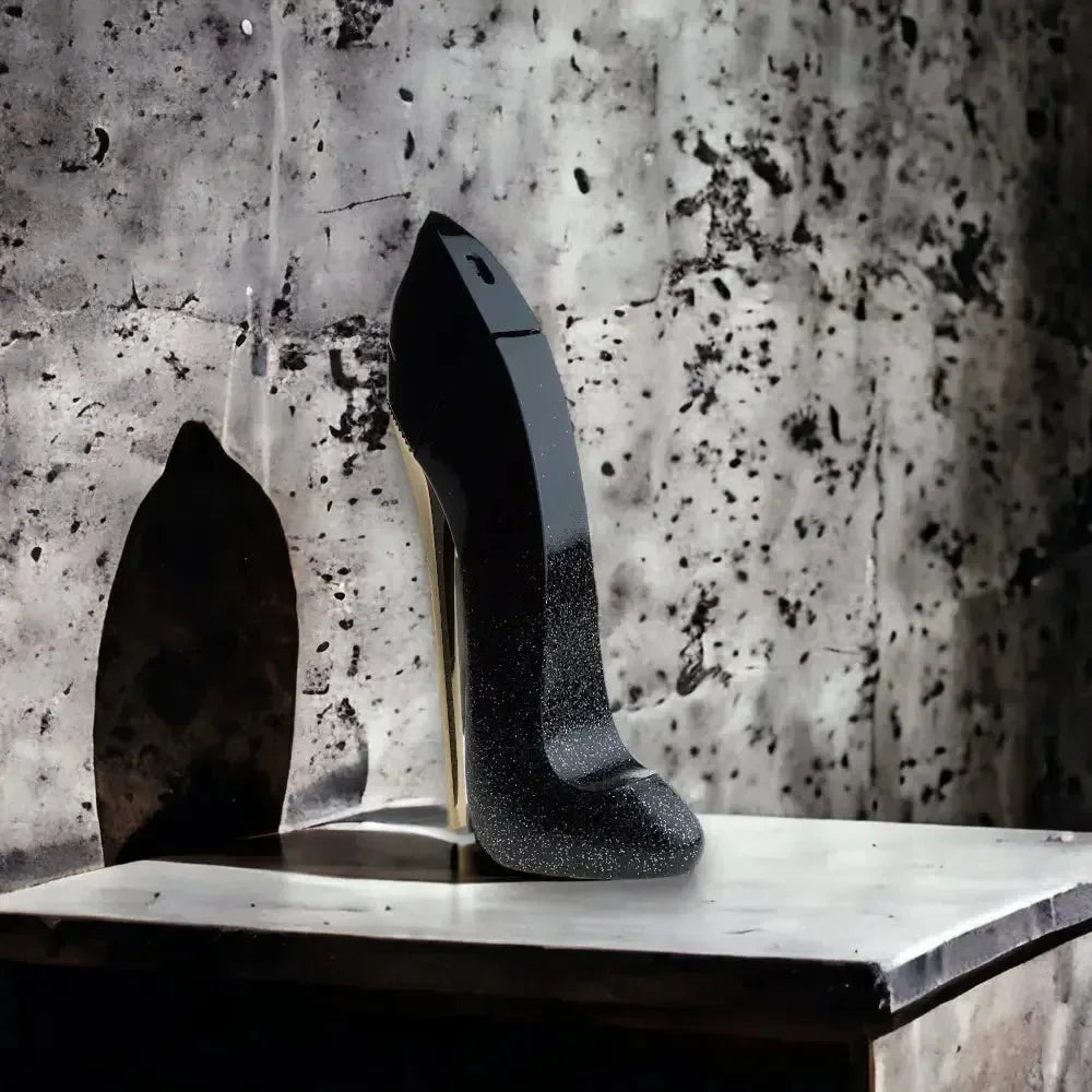 Eleganter schwarzer Parfumflakon in High Heel Form auf Marmoruntergrund vor Betonwand.