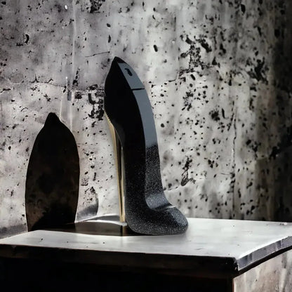 Eleganter schwarzer Parfumflakon in High Heel Form auf Marmoruntergrund vor Betonwand.