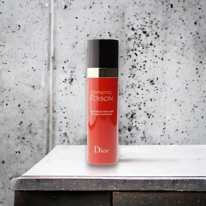 Roter Hypnotic Poison Deodorant Spray auf Tisch vor grauer Wand, luxuriöses Damenparfum