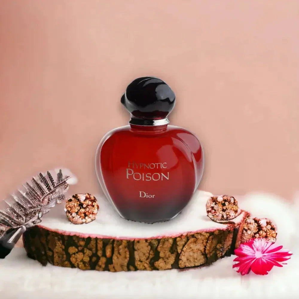 Rotes Damenparfum-Flakon Hypnotic Poison vor pastellfarbenem Hintergrund, dekoriert mit Blume und Holzscheibe