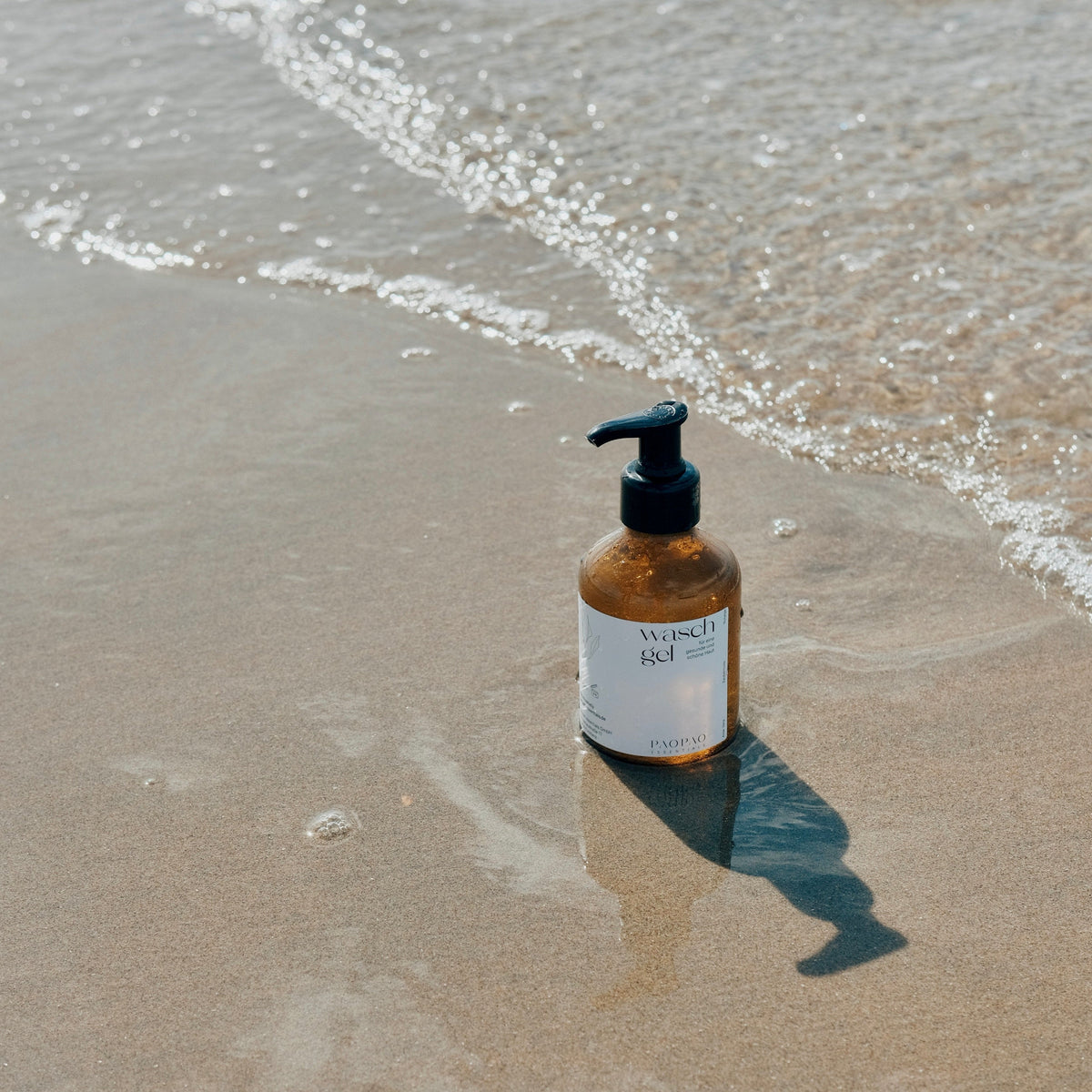paopao essentials Waschgel in einer braunen Glasflasche mit Pumpspender am Sandstrand.