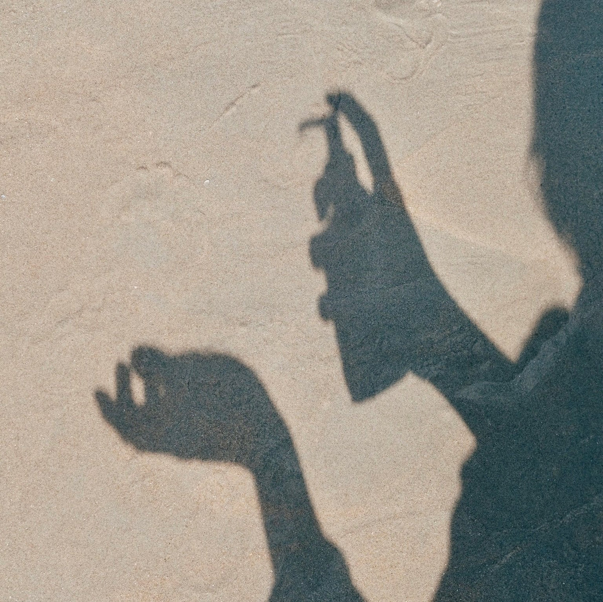 Schatten einer Hand mit einem Sprühflakon von paopao essentials auf hellem Sand.