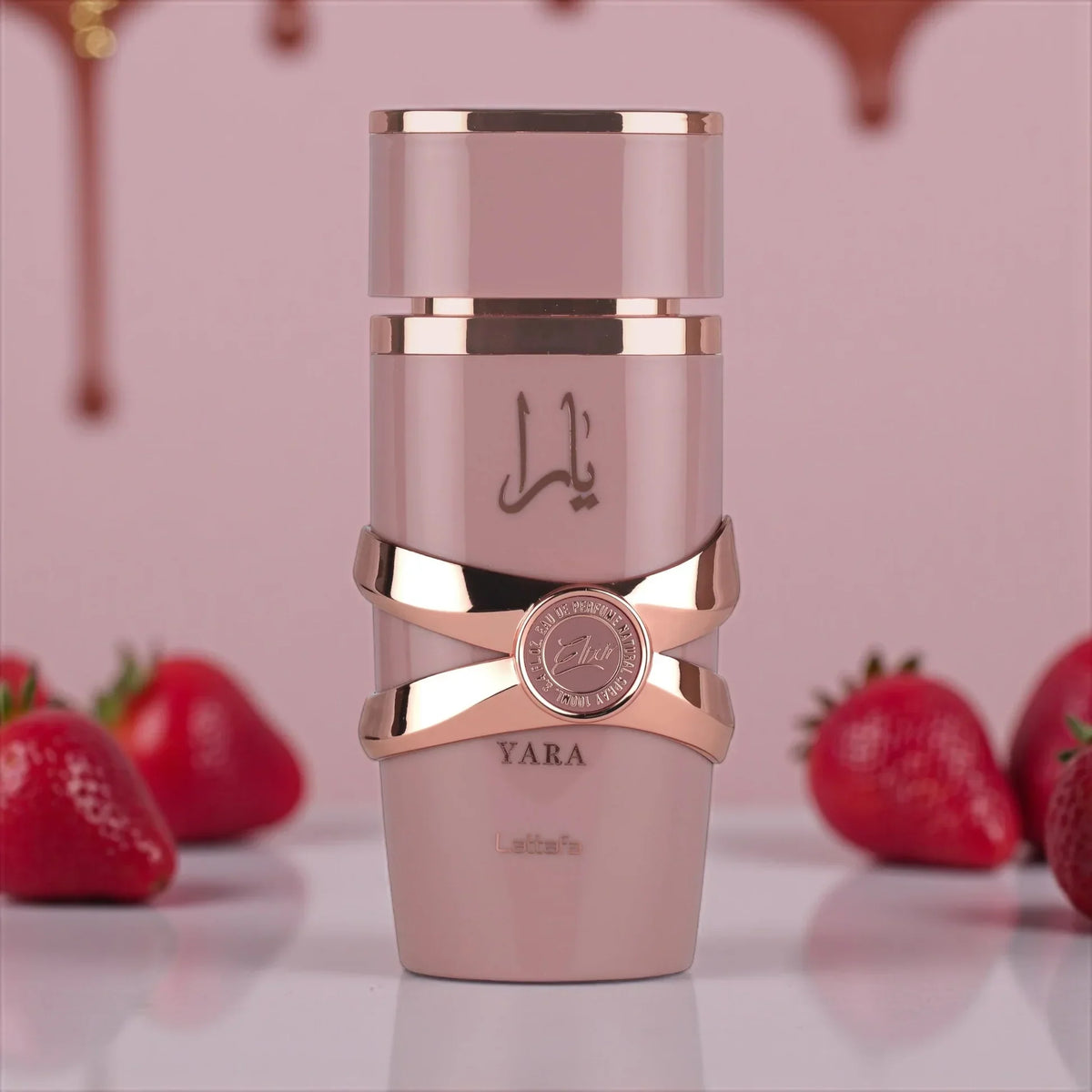 Eleganter Parfümflakon Yara Elixir vor rosa Hintergrund mit frischen Erdbeeren, luxuriöses Damenparfum