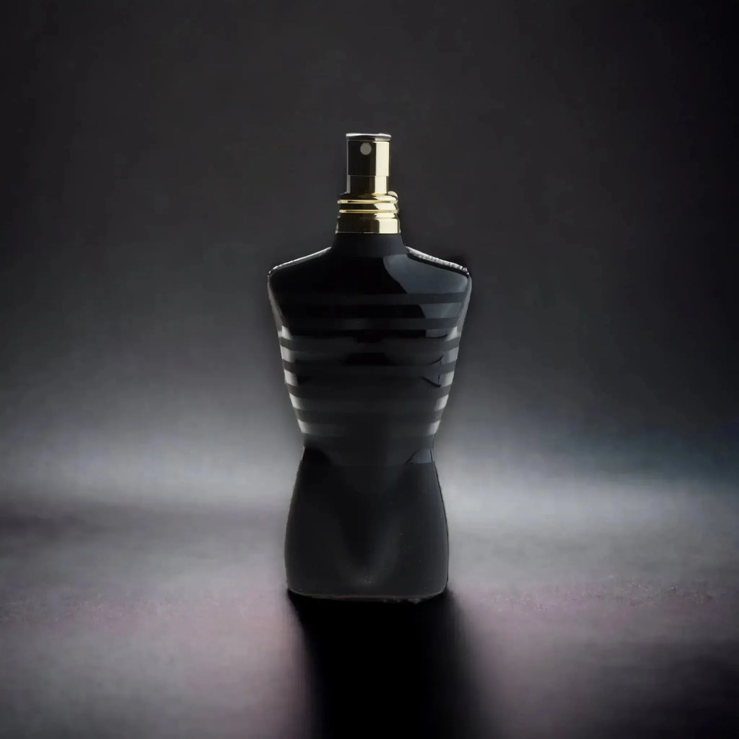 Schwarzer Parfümflakon in Torso-Form mit goldfarbenem Sprühkopf auf dunklem Hintergrund