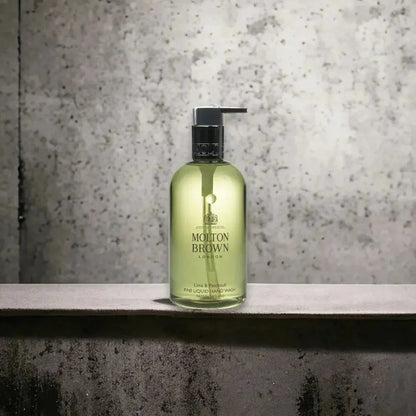 Molton Brown Lime Patchouli Handseife im transparenten Spender vor grauer Wand