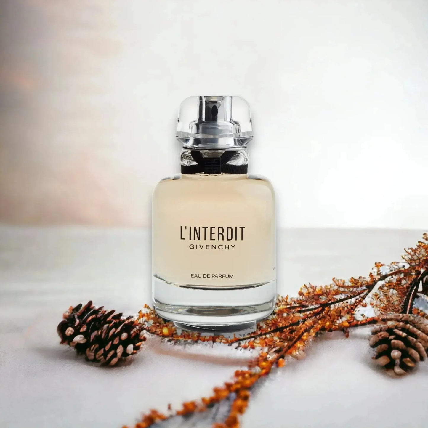 Luxuriöses Damenparfum L'Interdit Eau de Parfum Flakon, umgeben von Tannenzapfen und Blüten