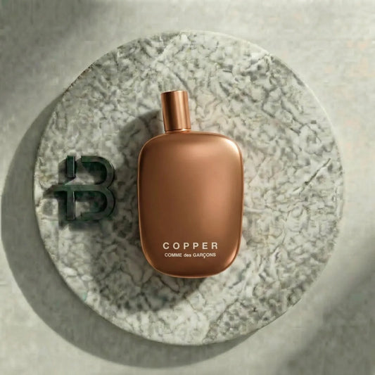 Kupferfarbenes Parfumflakon Comme des Garçons Copper auf rundem Marmortablett, Luxusduft