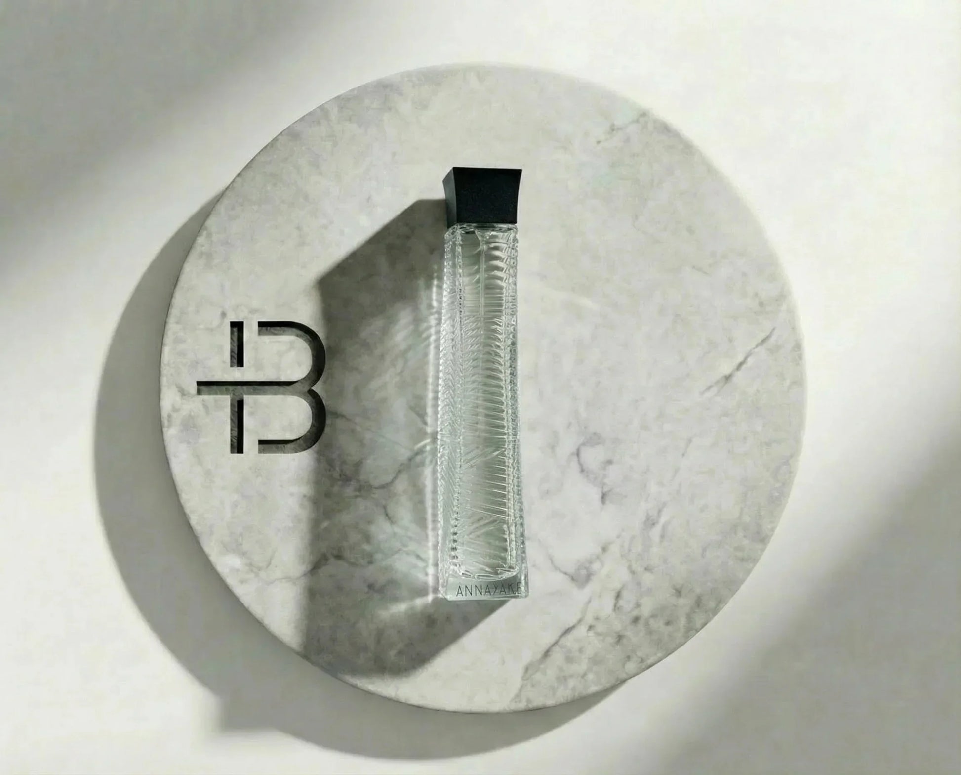 Eleganter Parfumflakon aus Glas mit schwarzem Deckel auf rundem Marmor-Untergrund, Luxusduft