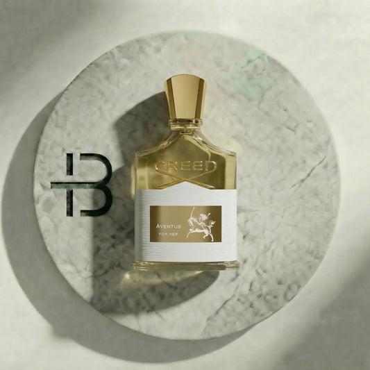 Luxuriöses Aventus for Her Parfumflakon mit goldenem Verschluss auf hellem Marmorteller