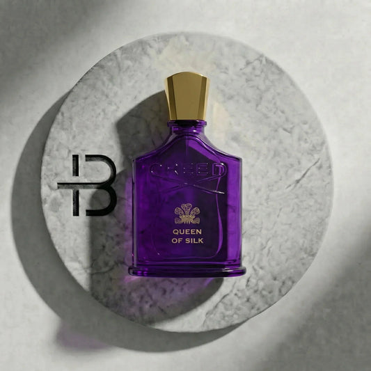 Lila Luxusparfum-Flakon mit goldenem Verschluss und der Aufschrift 'Queen of Silk' auf Marmorscheibe