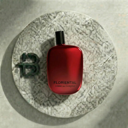Roter Flakon mit Aufschrift 'FLORIENTAL Comme des Garçons' auf heller Steinplatte, luxuriöses Parfüm.