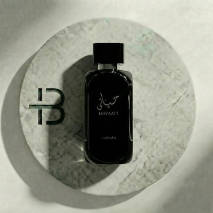 Elegantes, schwarzes HAYAATI Parfumflakon von Lattafa auf rundem Marmoruntergrund, arabische Schrift sichtbar.