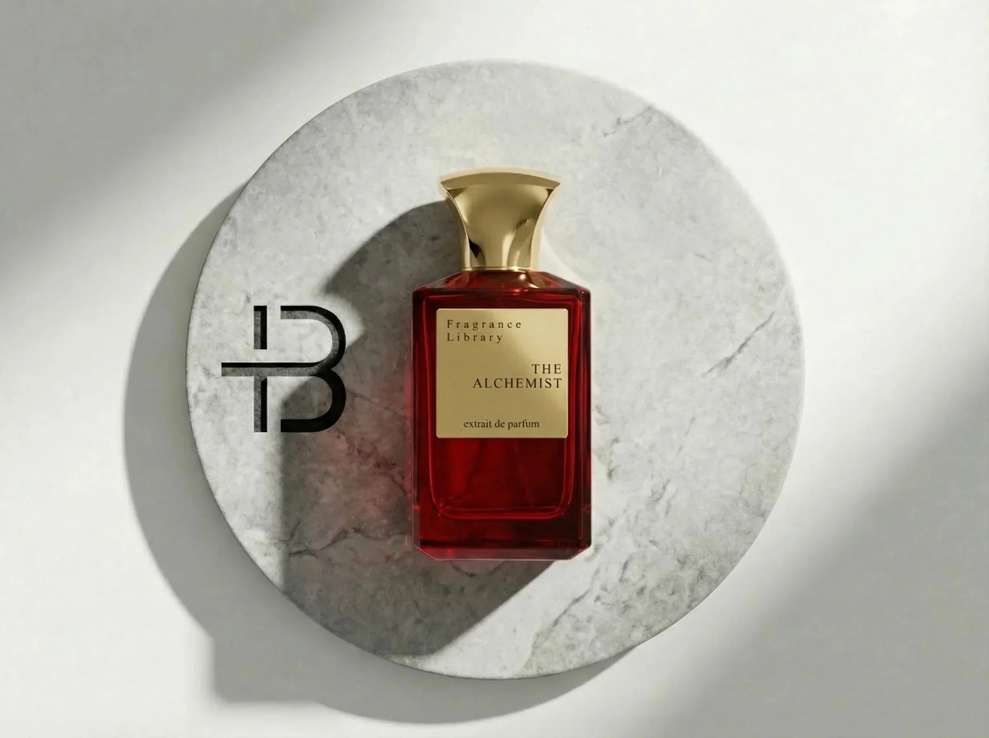 Roter Luxusparfumflakon mit goldener Kappe auf rundem Marmortablett, Aufschrift The Alchemist.