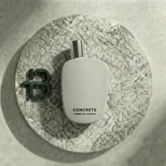 Graues Luxusparfum-Flakon Concrete Comme des Garçons auf rundem Marmortablett, minimalistisch