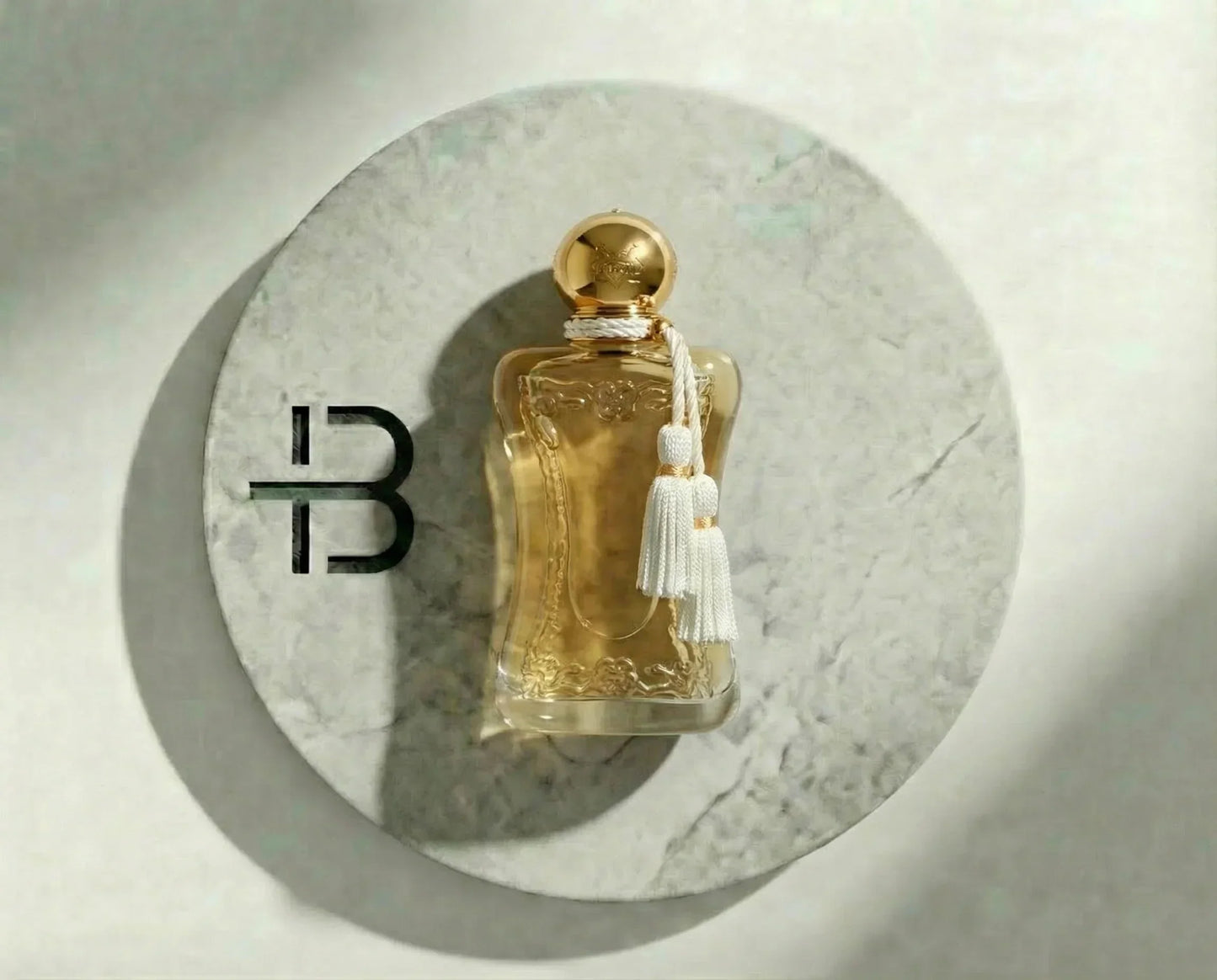 Luxusparfum Flakon mit goldener Kappe und weißer Quaste auf rundem Marmoruntergrund