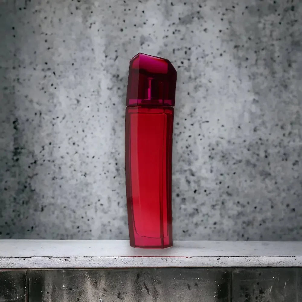 Ein rubinroter Flakon des Escada Magnetism Eau de Parfum vor einer grauen Betonwand.