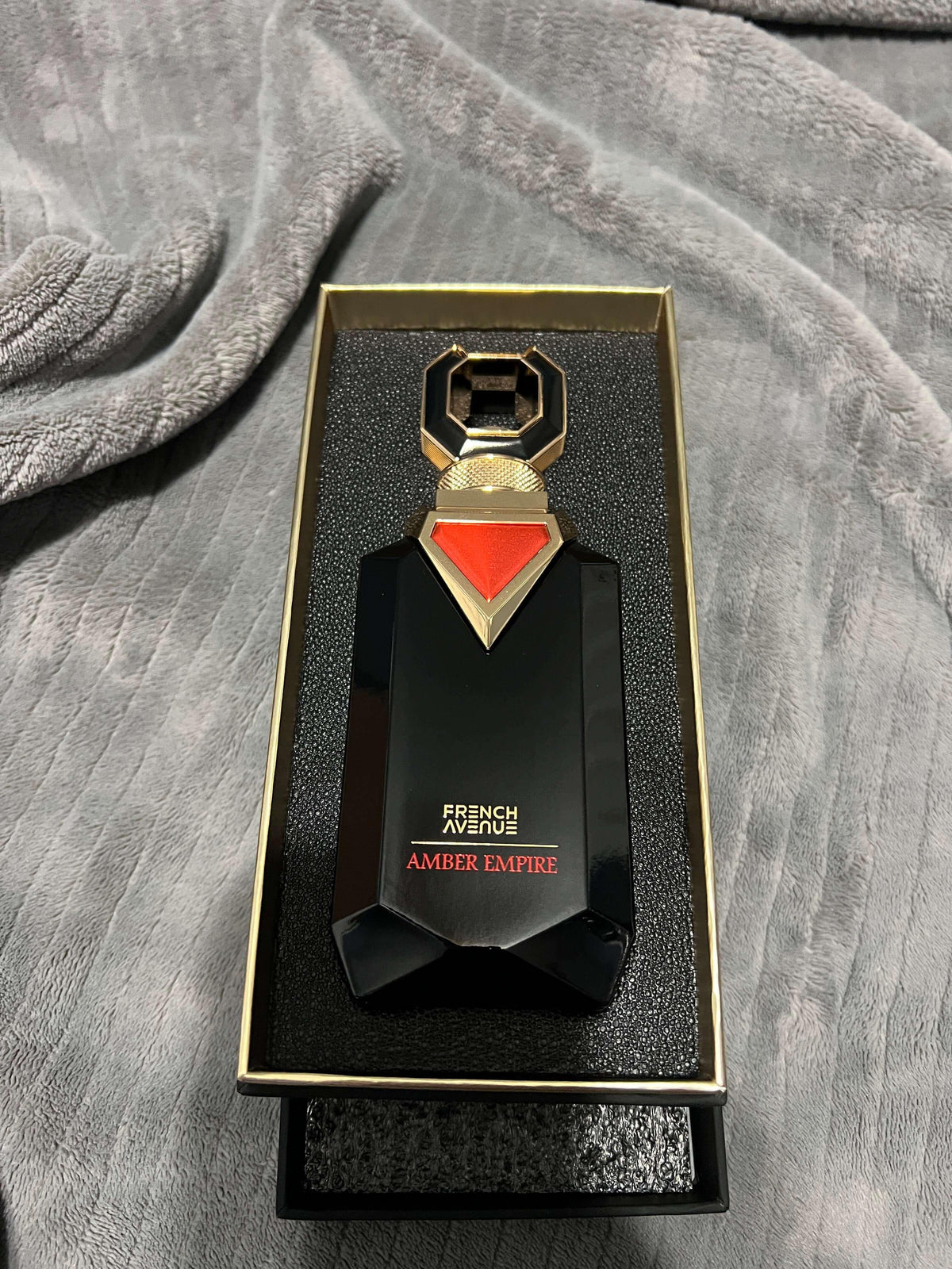 Luxuriöses Parfumflakon French Avenue Amber Empire in Geschenkbox auf grauem Stoff