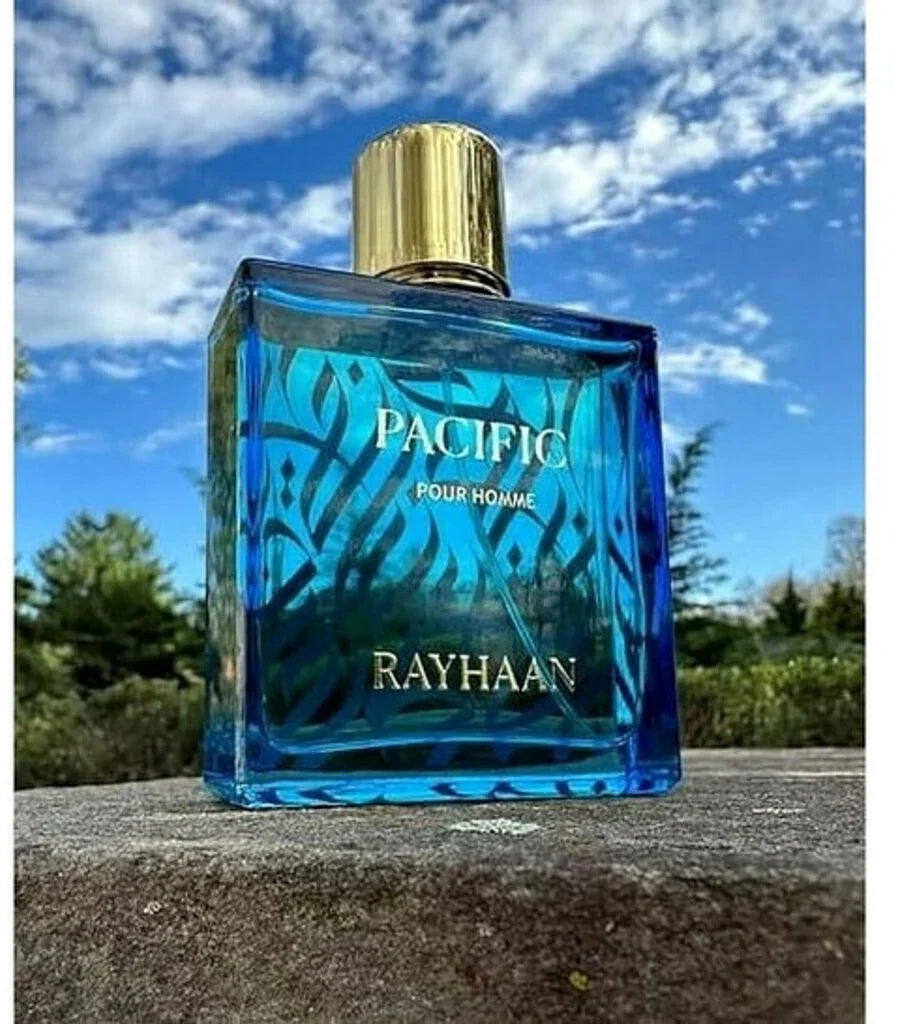 Blauer Parfumflakon Rayhaan Pacific Pour Homme, 100ml, mit Goldverschluss vor blauem Himmel, Herrenduft.