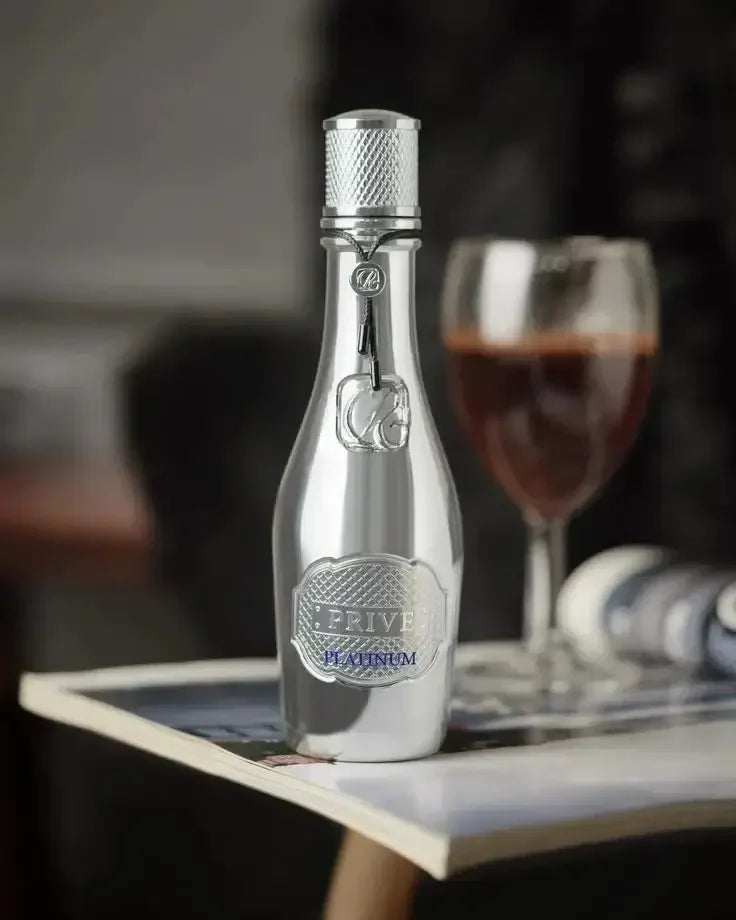 Luxuriöses Parfum Prive Platinum in silberner Flasche auf Tisch, Glas Rotwein im Hintergrund