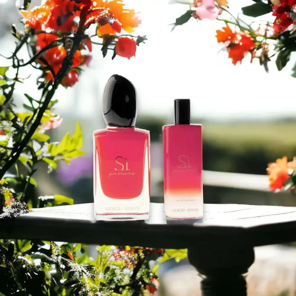 Zwei Si Passione Eau de Parfum Flakons, leuchtend rot, auf Holztisch im Garten, umgeben von Blüten.